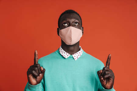 Young african man in a white medical mask isolated on red background, presenting copy space
