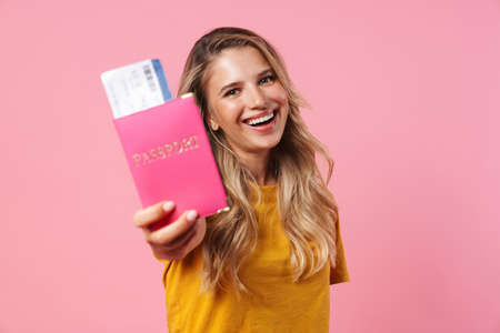 Image of happy blonde girl showing passport with tickets isolated over pink backgroundの写真素材