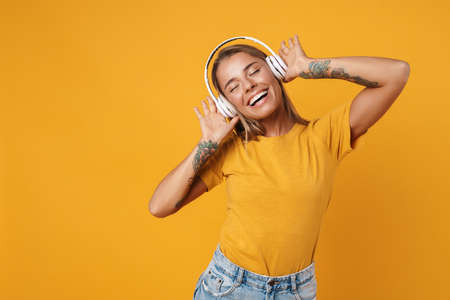 Image of blonde joyful woman smiling and listening music with headphones isolated over yellow backgroundの写真素材