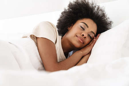 Smiling beautiful young african woman sleeping in bed, eyes closed