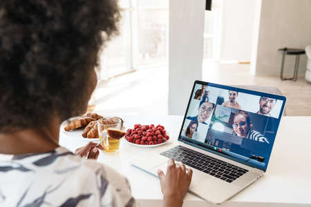 Cheerful beautiful woman using laptop for a video call while having breakfast in modern kitchen,...