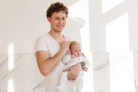 Happy young father holding his little baby son while standing indoors