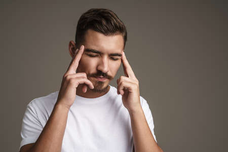 Image of unhappy unshaven guy with headache rubbing his temples isolated over grey backgroundの写真素材