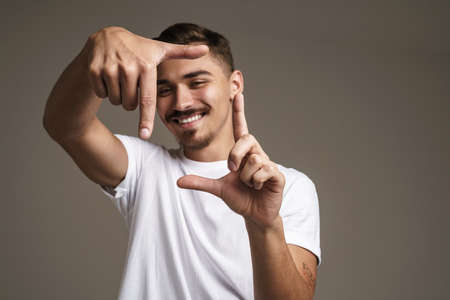 Image of cheerful unshaven guy showing photo frame gesture isolated over grey background