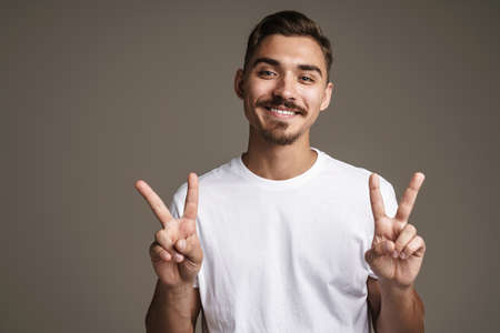 Image of cheerful unshaven guy showing peace sign gesture isolated over grey background
