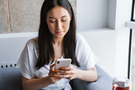 Happy girl reading a message on a smart phone while sitting on a couch at homeの写真素材