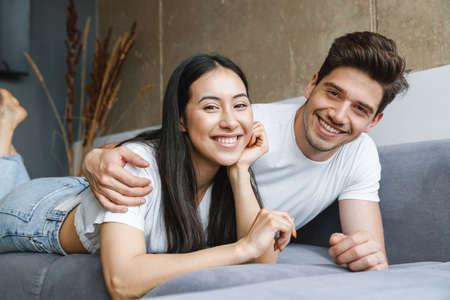 Beautiful young happy couple laying on couch, embracingの写真素材