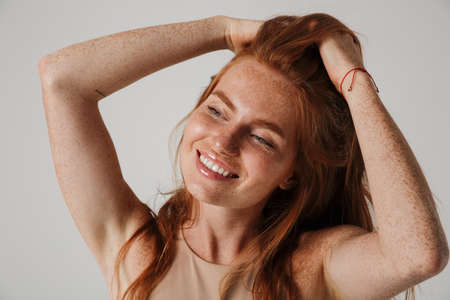 Close up of a young smiling beautiful woman with long red hair isolated over gray