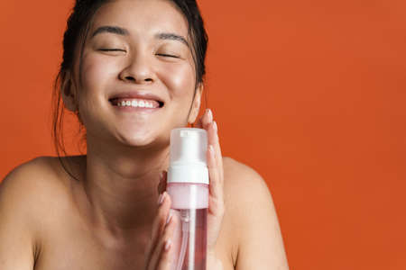 Image of smiling shirtless asian girl posing with cleansing foam isolated over orange background