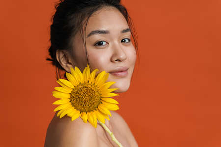 Image of shirtless asian girl smiling while posing with sunflower isolated over orange backgroundの写真素材