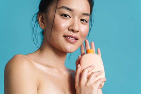 Image of pleased shirtless asian girl posing with shampoo isolated over blue background