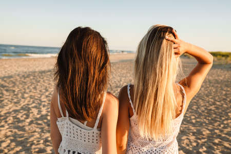 Two young caucasian women standing with their back while walking on beachの写真素材