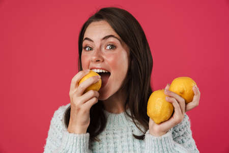 Image of happy beautiful girl holding and eating lemons isolated over pink backgroundの写真素材