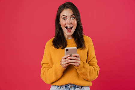 Excited young woman holding mobile phone, celebrating isolated over pink backgroundの写真素材