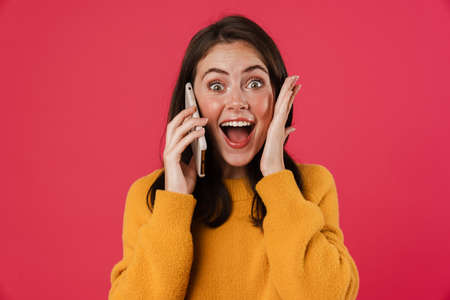 Portrait of a pretty joyful girl talking on mobile phone isolated over pink backgroundの写真素材