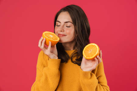 Image of happy caucasian girl smiling while smelling orange isolated over pink backgroundの写真素材