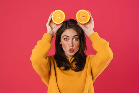 Image of amusing caucasian girl making fun with orange isolated over pink backgroundの写真素材