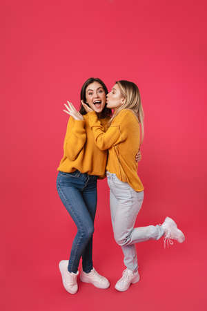 Full length portrait of two young female friends standing over pink backgroundの写真素材