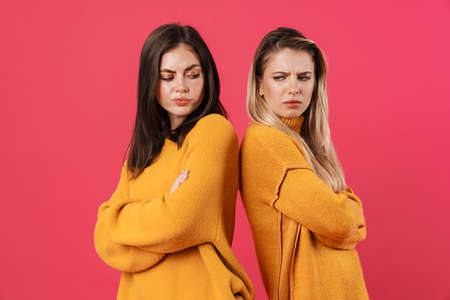Image of resentful beautiful women standing back to back isolated over pink backgroundの写真素材
