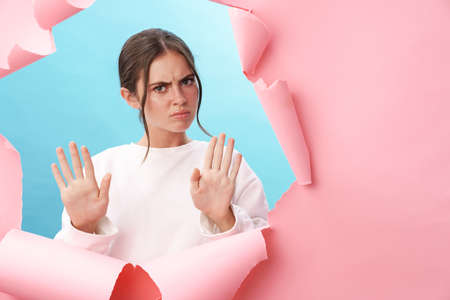 Caucasian young strict woman frowning and doing stop gesture with hands isolated through pink...