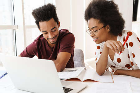 Beautiful couple sitting at the kitchen with laptop, working togetherの写真素材