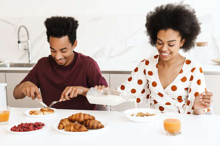 Happy young african couple having tasty breakfast while sitting at the kitchen tableの写真素材