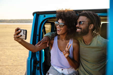 Young couple in love making selfie using smart phone while sitting on a back of carの写真素材
