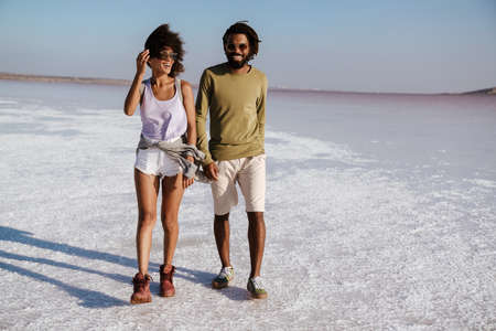 Loving young african couple walking along the seashore, holding handsの写真素材