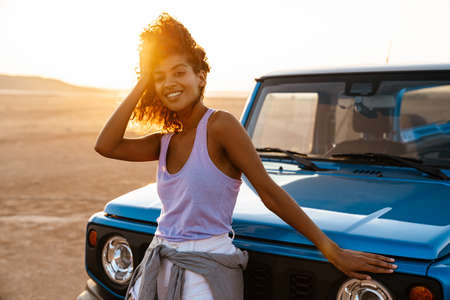 Image of cheerful african american woman smiling while travelling with car on desertの写真素材