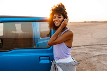 Photo of an african american woman standing at her car on beach at sunrise