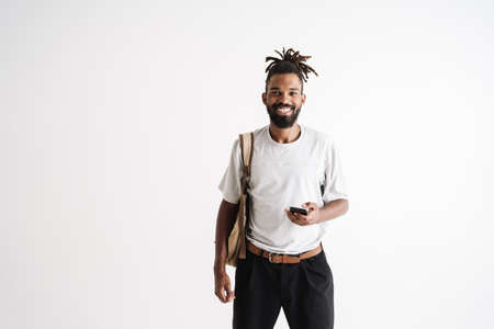 Photo of joyful african american guy smiling and using mobile phone isolated over white background