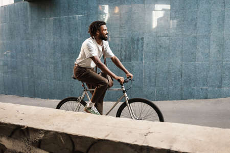 Happy african american guy smiling while riding bicycle at city streetの写真素材