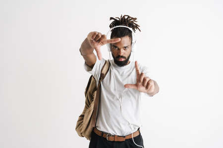 Photo of serious african american guy in headphones showing frame gesture isolated over white wall