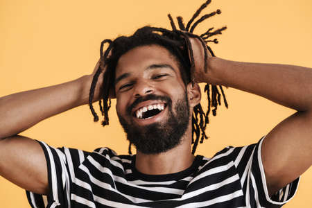 Photo of cheerful african american guy looking and laughing at camera isolated over yellow backgroundの写真素材