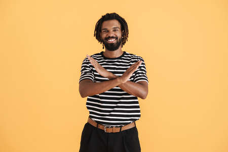 Photo of cheerful african american guy showing stop gesture isolated over yellow background
