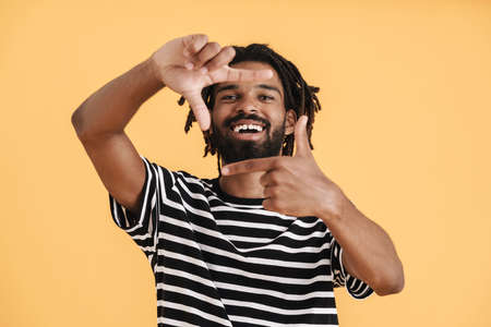 Photo of cheerful african american guy showing photo frame gesture isolated over yellow background