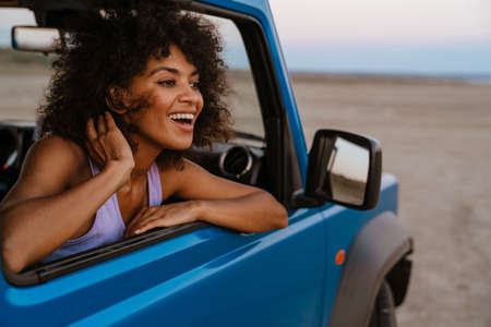 Image of cheerful african american woman smiling while travelling in car on desertの写真素材