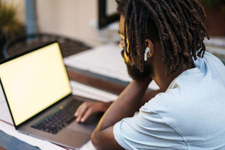 Focused african american guy in earphones working with laptop while sitting in cafe outdoors