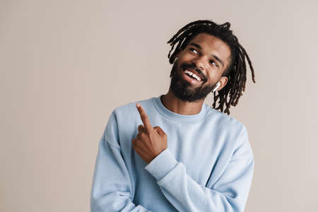Cheerful african american guy in earphones pointing finger upward isolated over white background