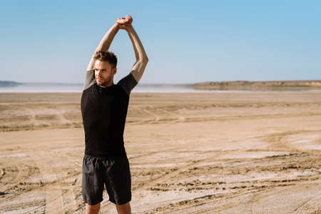Motivated focused young sportsman exercising at the beach, stetchingの写真素材