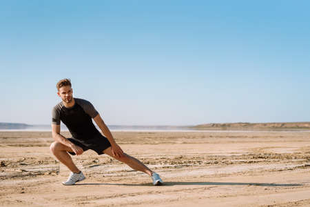 Motivated focused young sportsman exercising at the beach, stetchingの写真素材