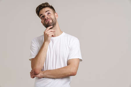 Confused handsome unshaven guy thinking and looking upward isolated over grey background