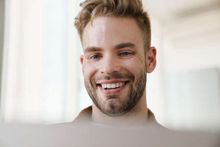 Handsome cheerful guy working with laptop and smiling at homeの写真素材