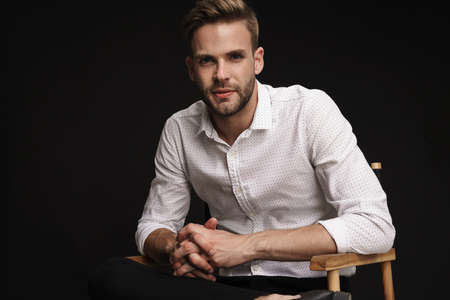 Handsome confident businessman sitting in armchair isolated over black background