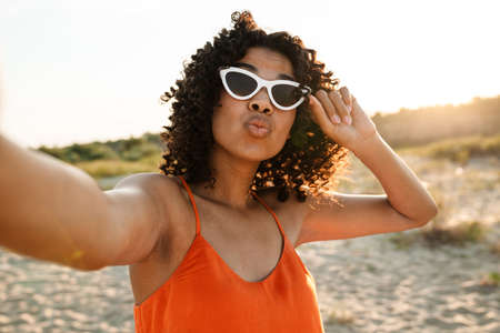 Smiling young african woman taking a selfie at the beach, wearing sunglasses