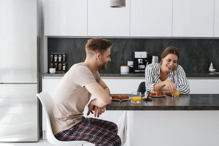 Young beautiful caucasian couple sitting at table while having breakfast at homeの写真素材