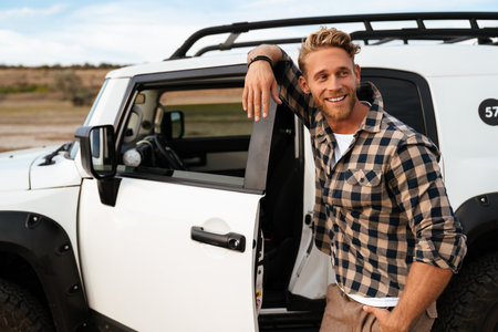 Handsome confident young man posing while standing at his car door at the beach