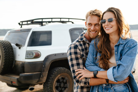 Beautiful young smiling couple while bonding to each other and leaning at their car