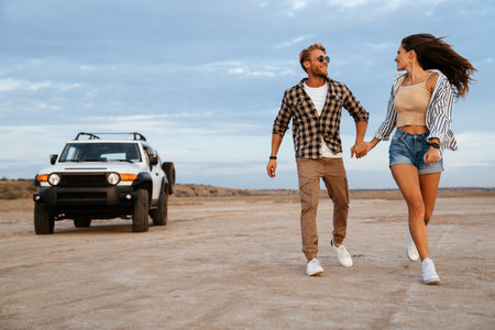 Young happy loving couple outdoors at beach near car walking, embracing, holding hands