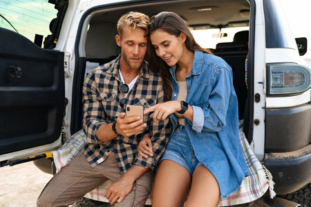 Beautiful couple sitting at the back of car and using smart phones